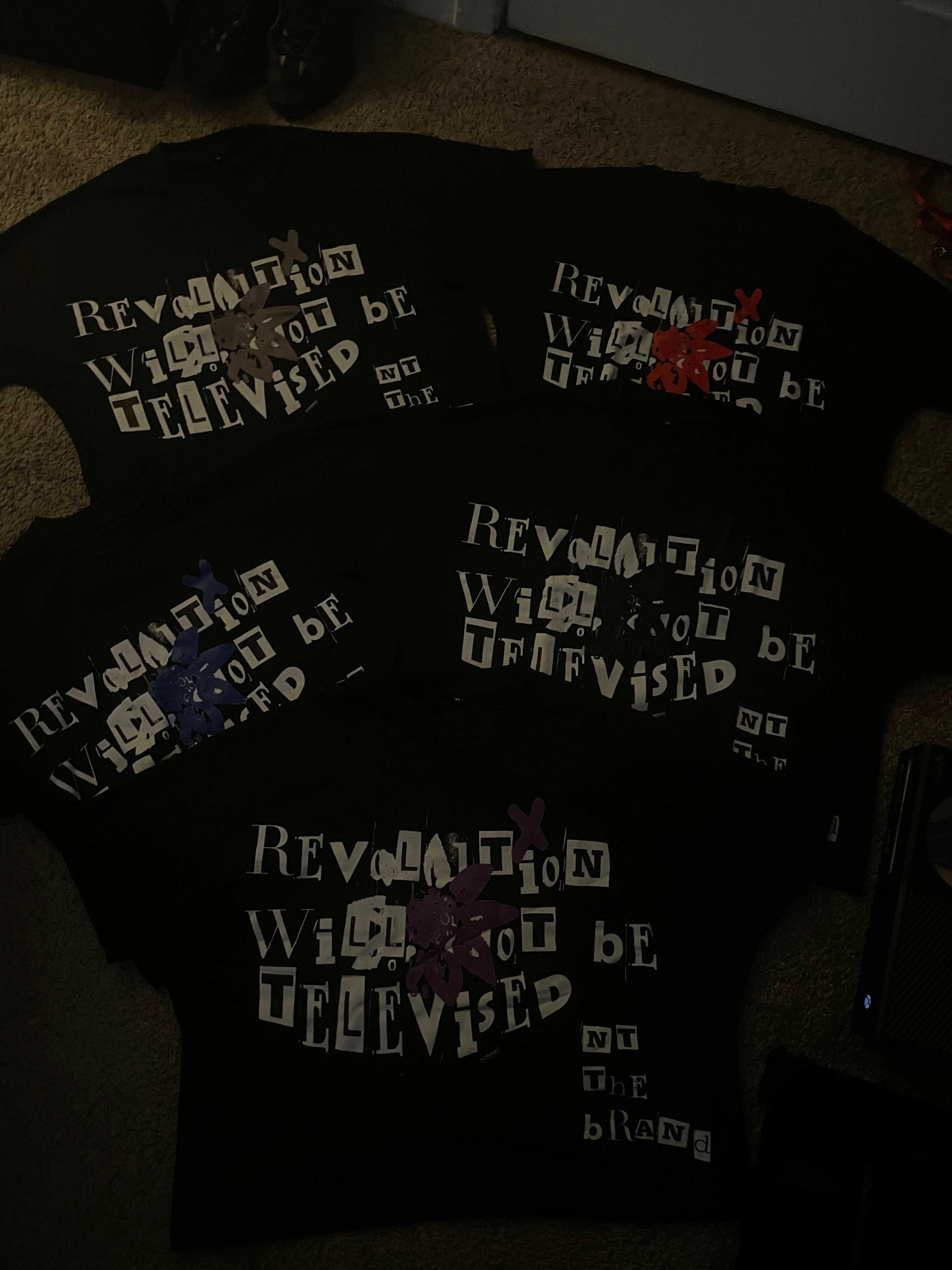Set of black Revolution bundle t-shirts with colorful flower x designs and white text saying "Revolution will not be televised" arranged in a fan shape on the floor