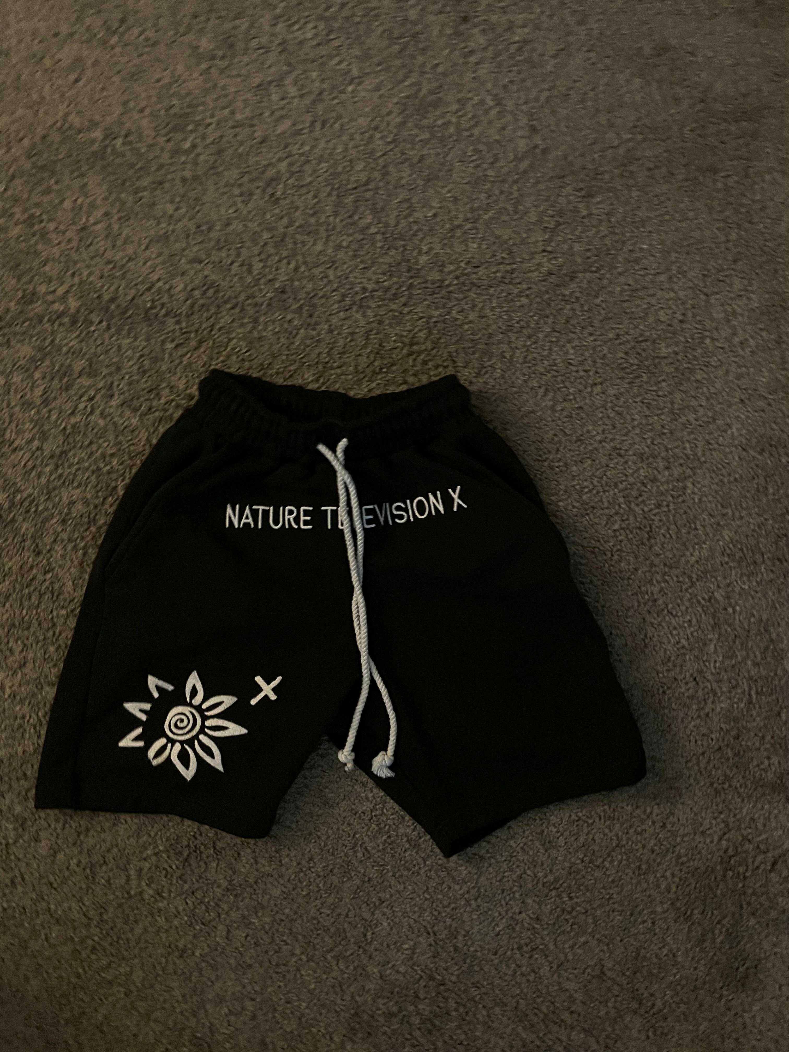 Black men's WISE FLOWER X shorts with white embroidered logo and drawstring waistband on gray carpet