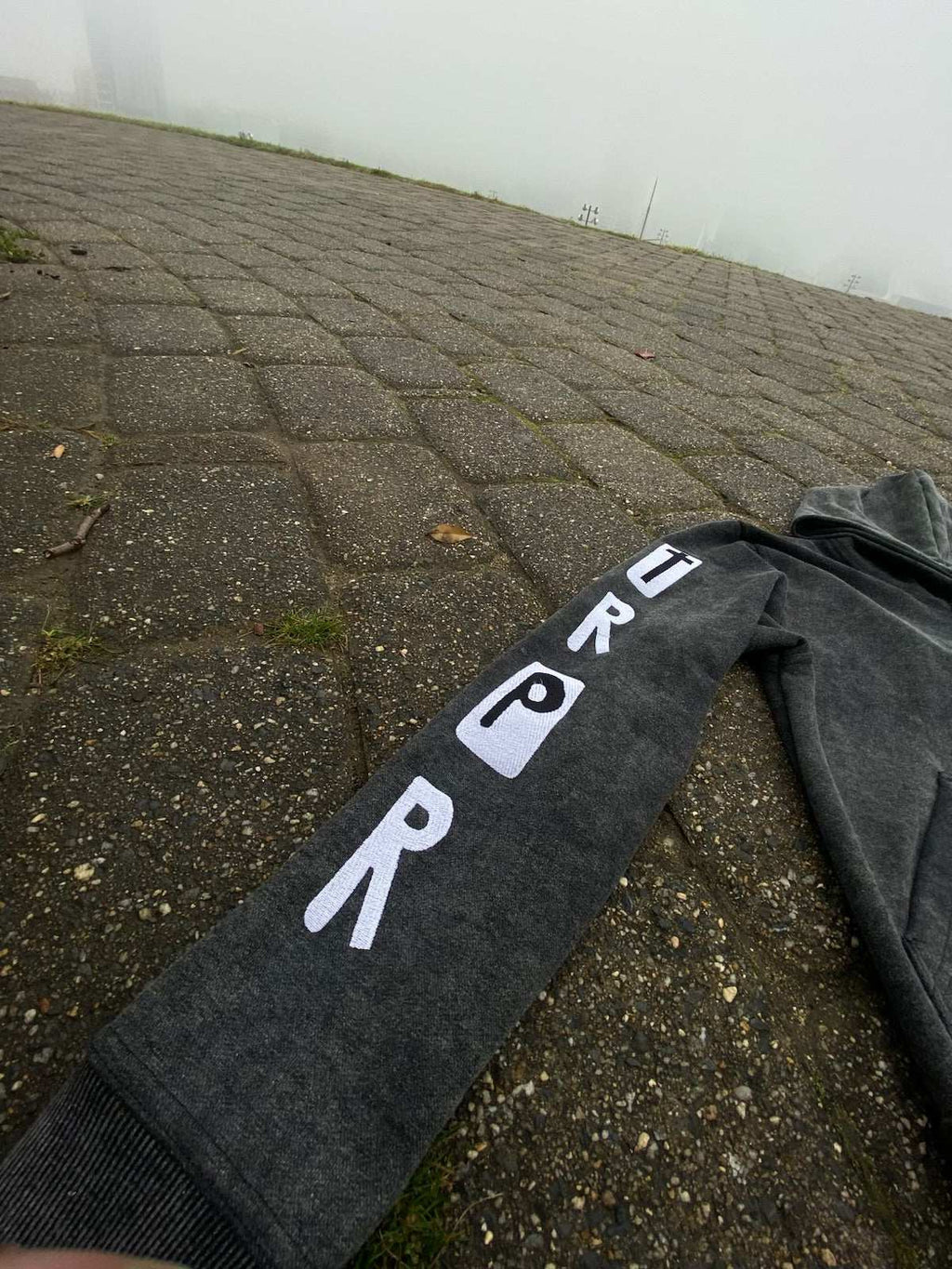 RPRT Hoodie Jacket dark grey with puff print embroidery on sleeve laid on pavement outdoors