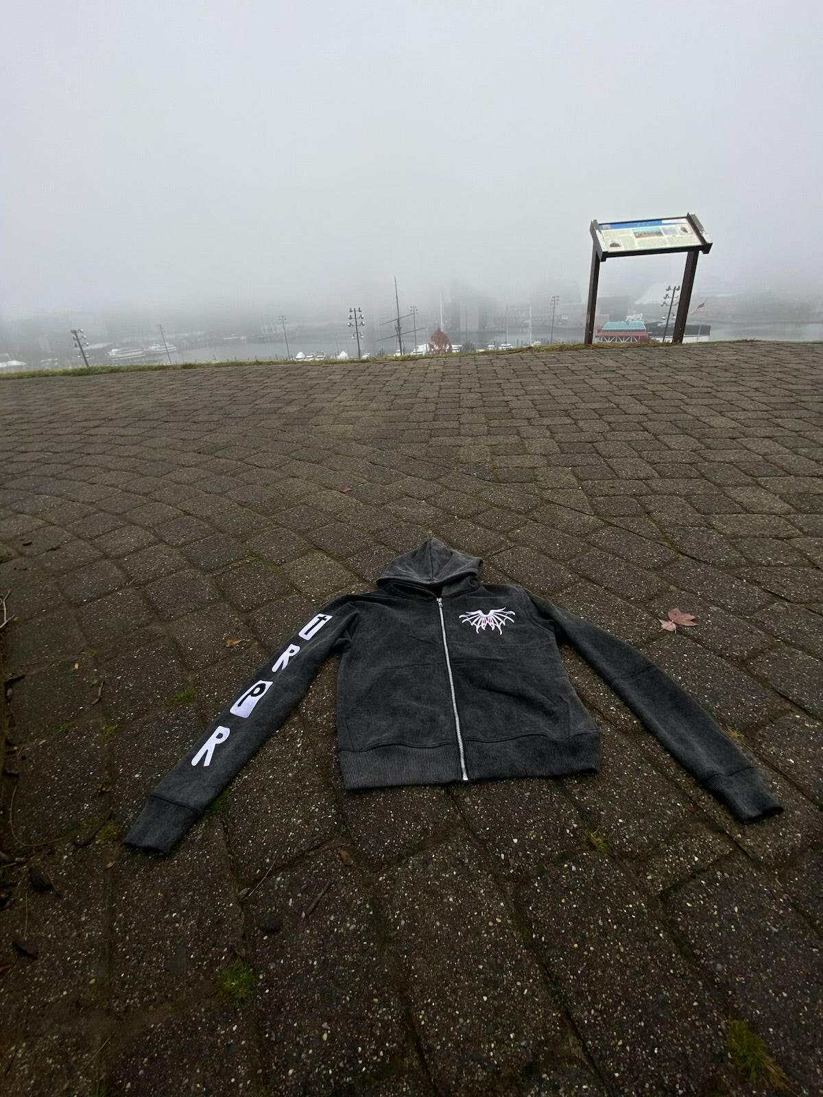 RPRT Hoodie Jacket black zip-up with puff print and embroidery on sleeve and chest placed on outdoor pavement