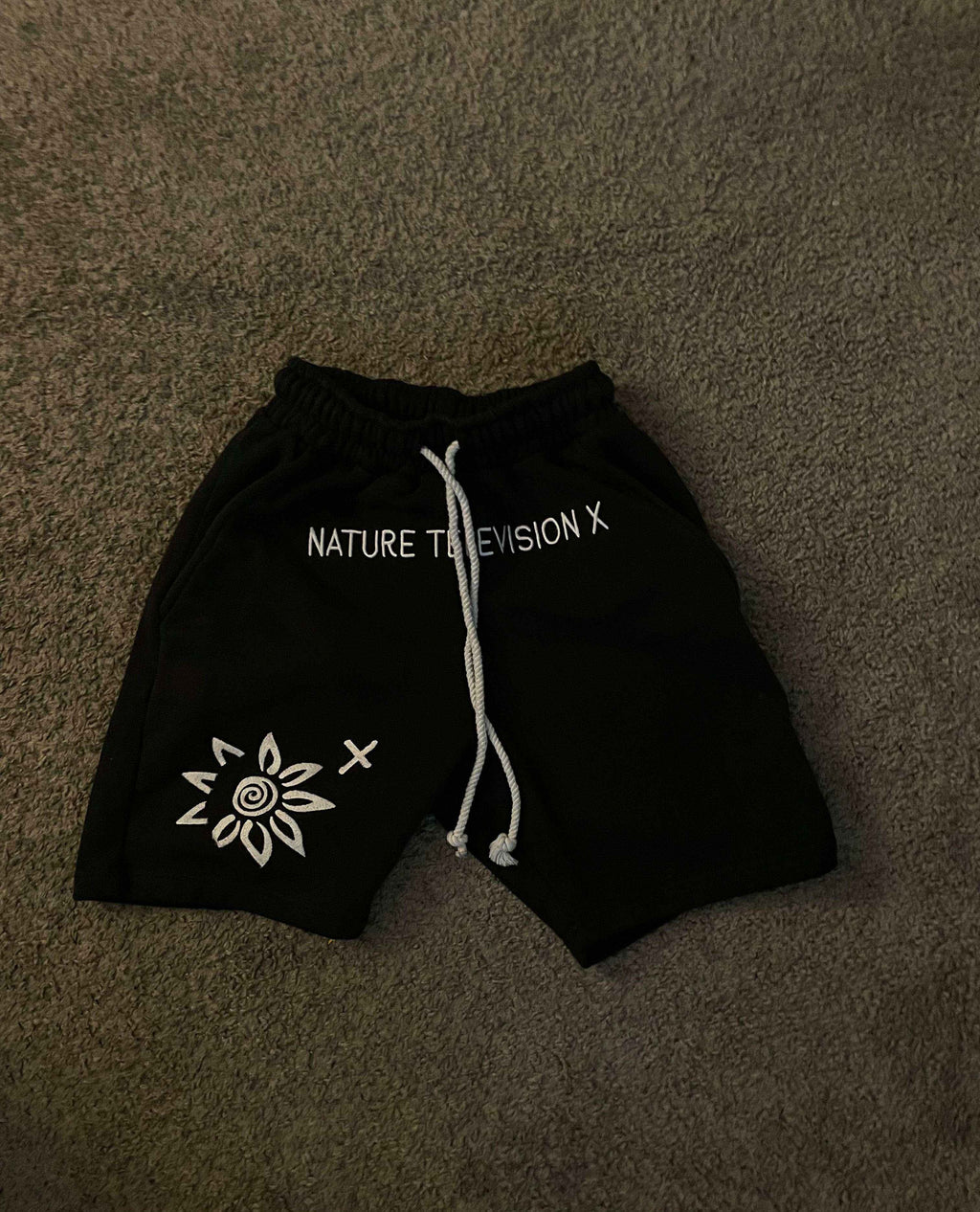 Black WISE FLOWER X men's shorts with white embroidered design and drawstring waistband