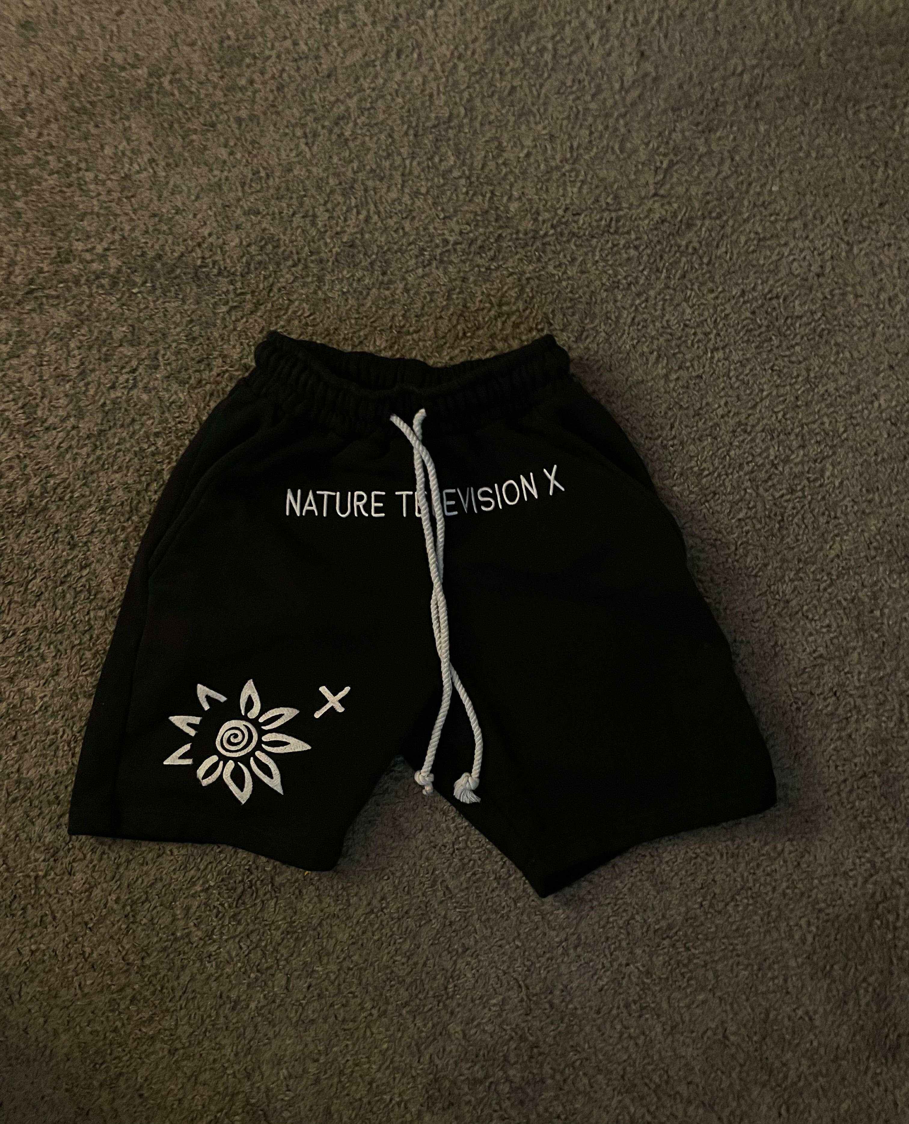 Black WISE FLOWER X men's shorts with white embroidered design and drawstring waistband