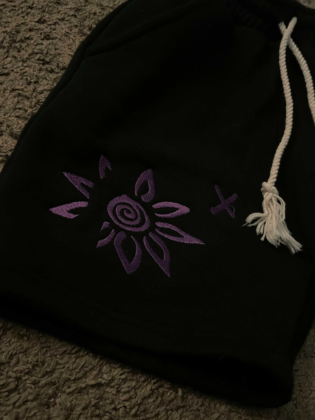Black shorts with purple embroidered Wise Flower X design and white drawstring rope